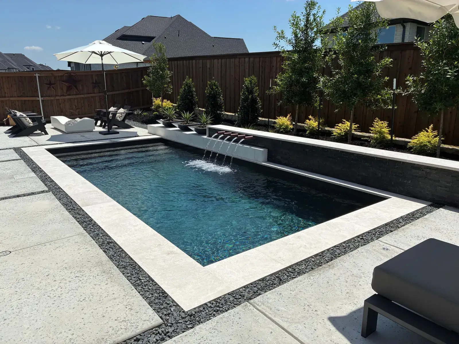 Rectangular pool with a sheer-descent water feature and travertine-style coping